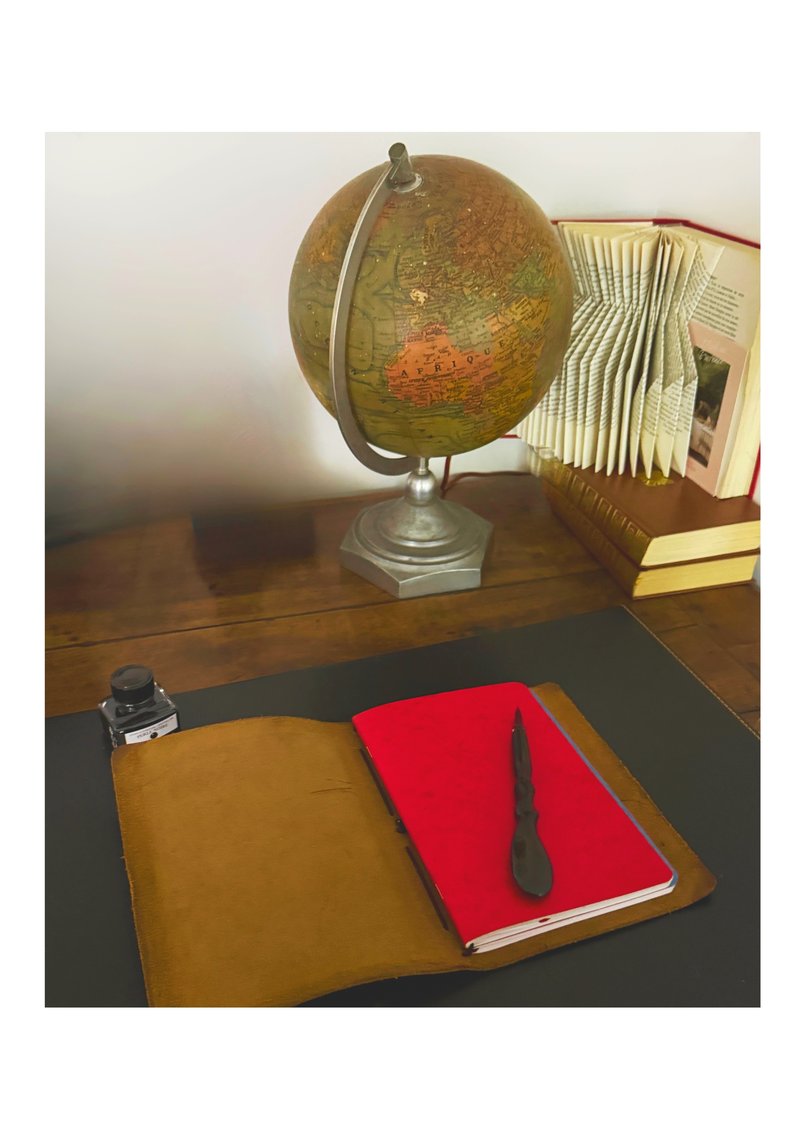 Étui en cuir ouvert avec carnet à couverture rouge et porte-plume, sur un bureau ancien avec globe terrestre et livres